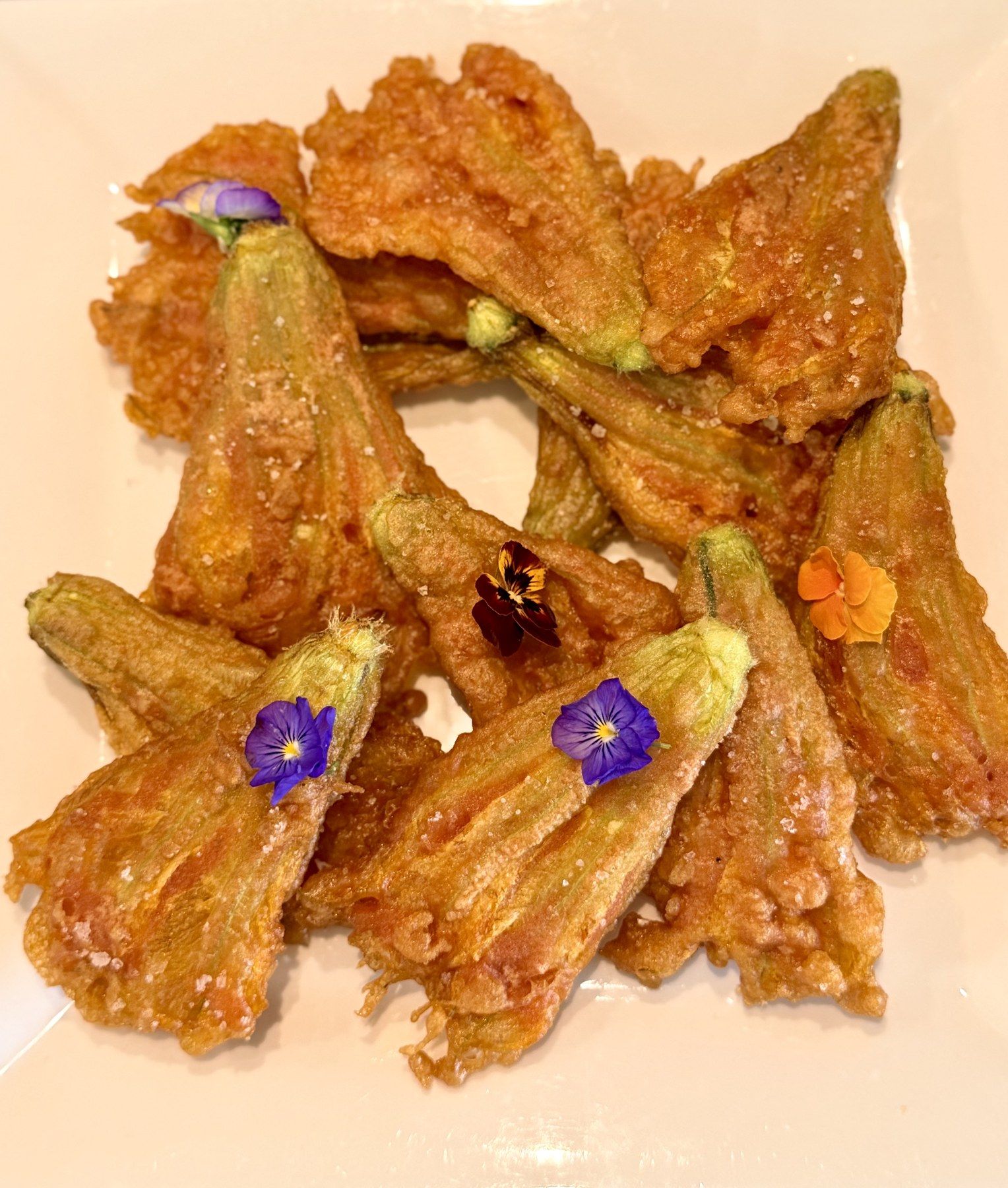 Crisp courgette-flower fritters finished with edible pansies.