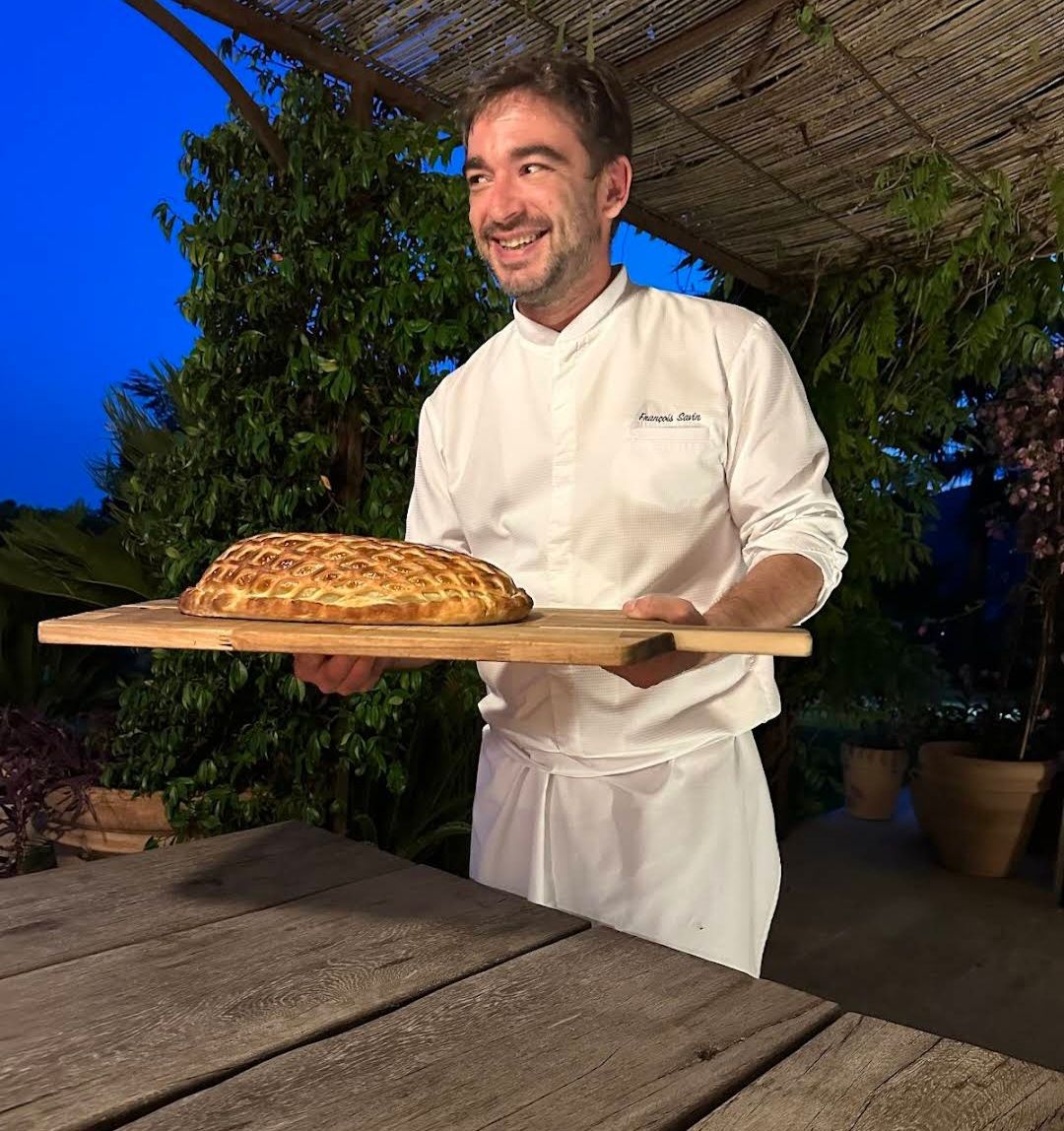 Chef François Savin under a pergola, holding a beef Wellington.