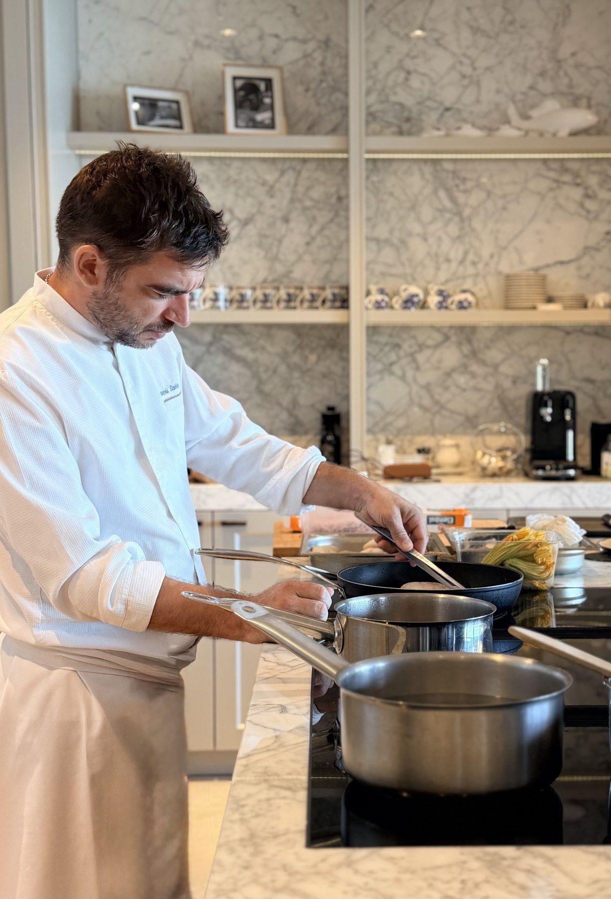 Chef François Savin at the stove of a marble villa kitchen, courgette flowers at hand.