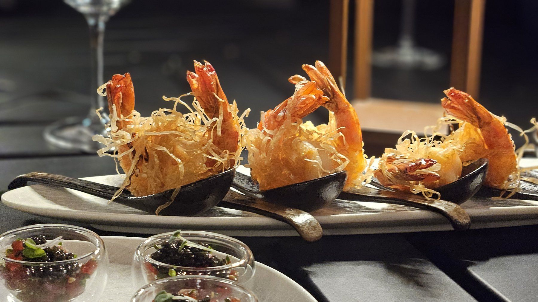 Crisp kadaif-wrapped prawns served in dark spoons, with caviar tartare bowls in the foreground.