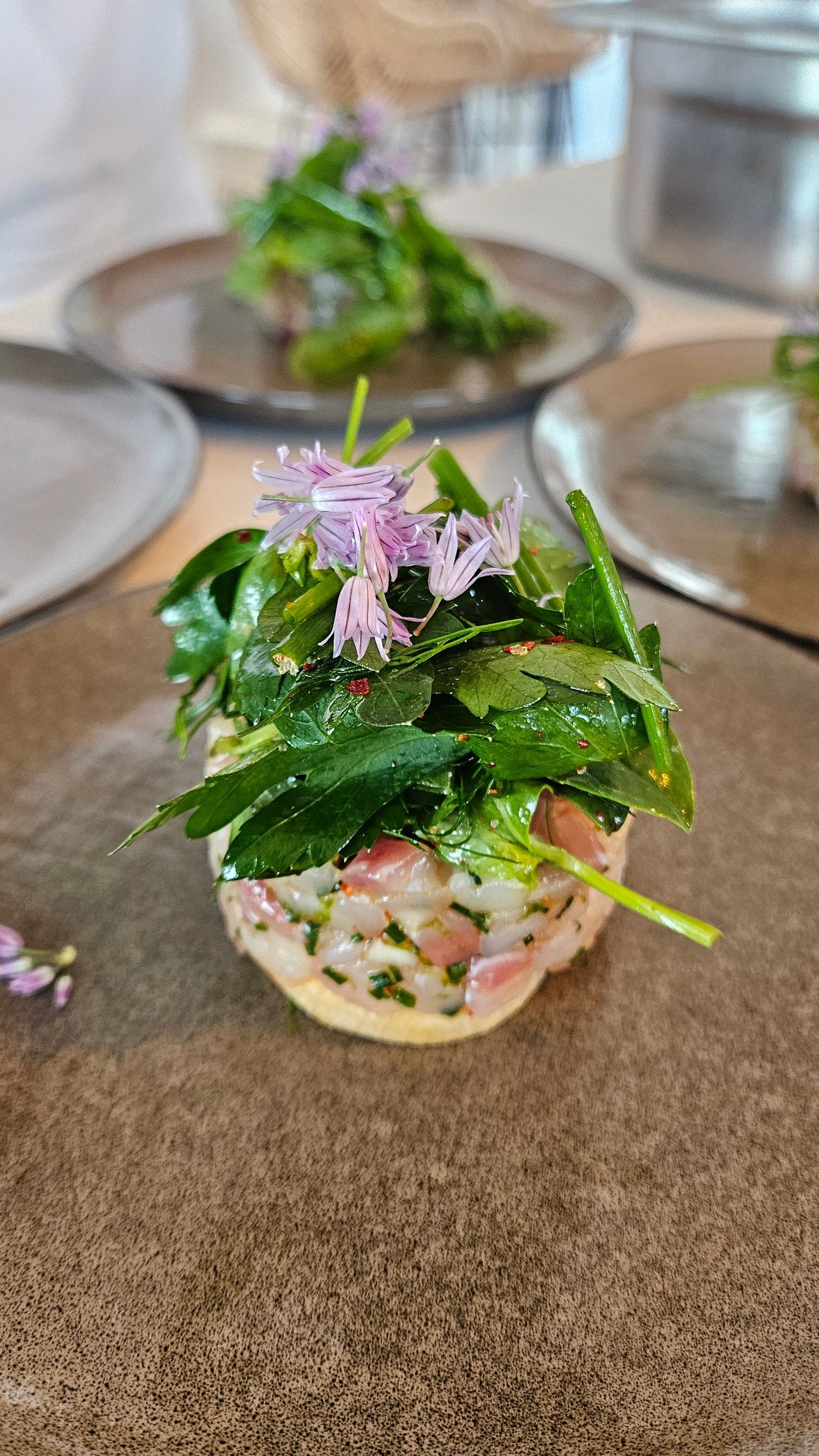 A fish tartare under a tangle of garden herbs and chive flowers.