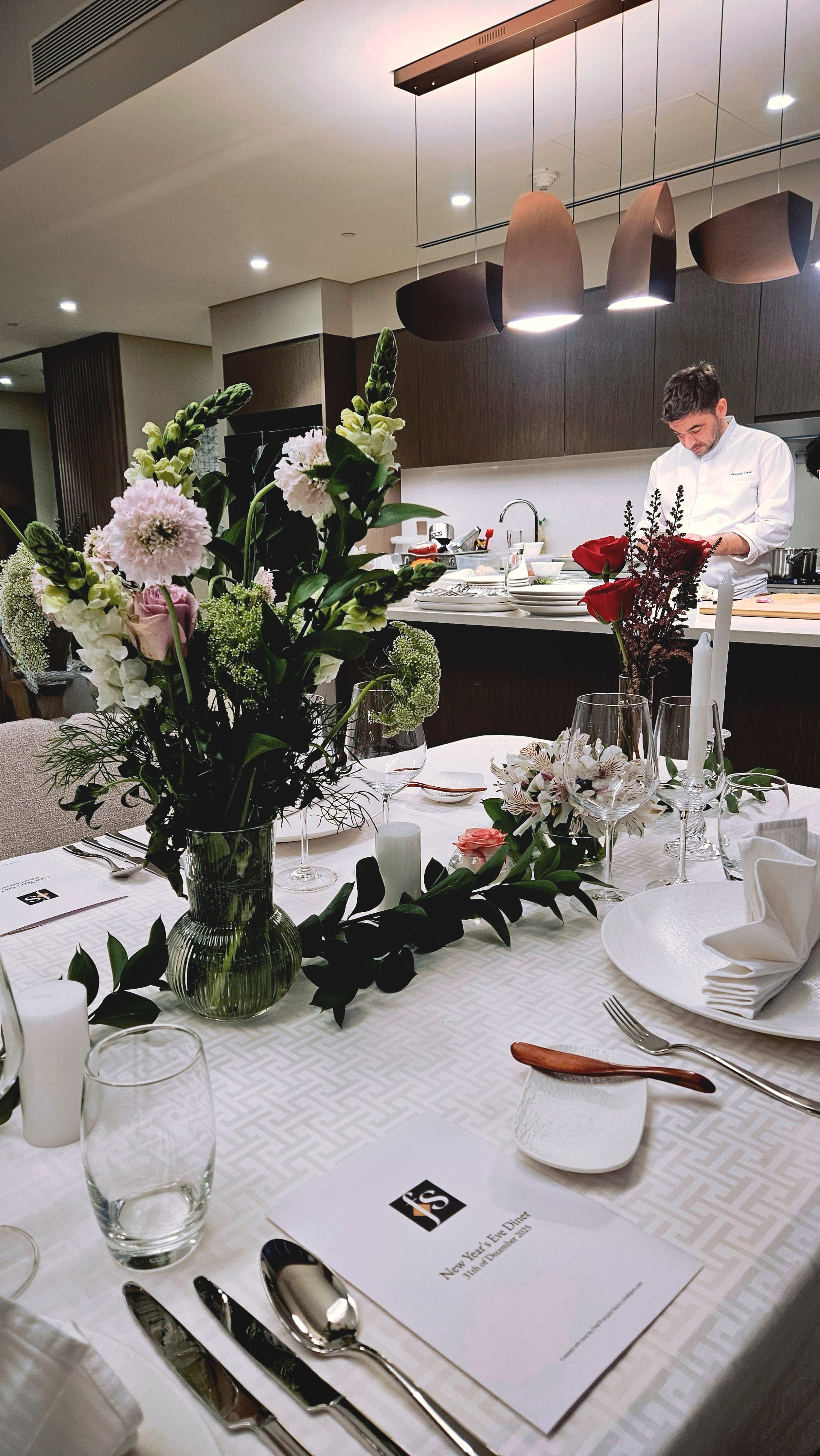 A dressed dining table set for the evening, candles and flowers, the Dubai skyline beyond the glass.