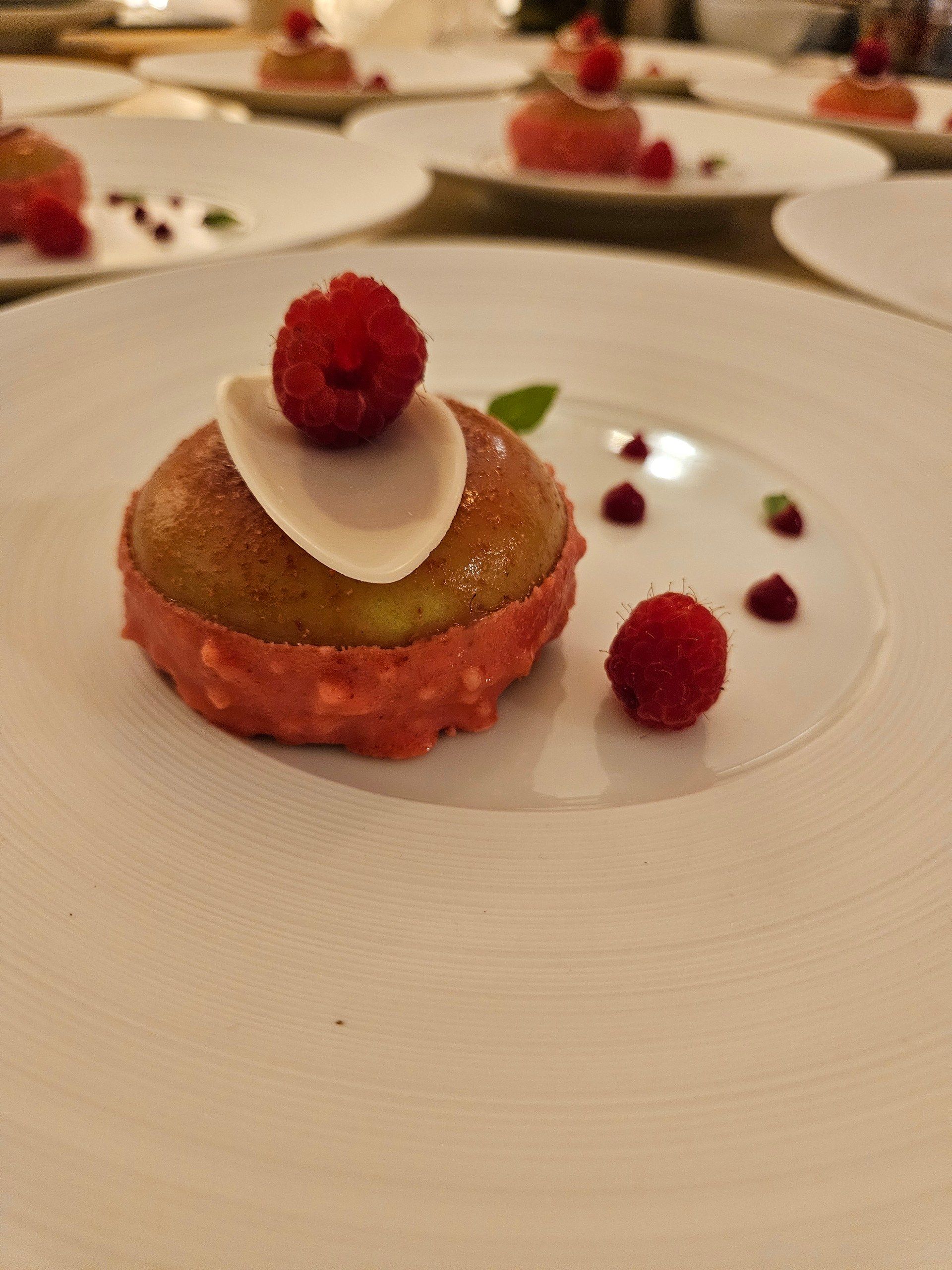 A raspberry dessert, built on the fruit in season, plated on white porcelain.
