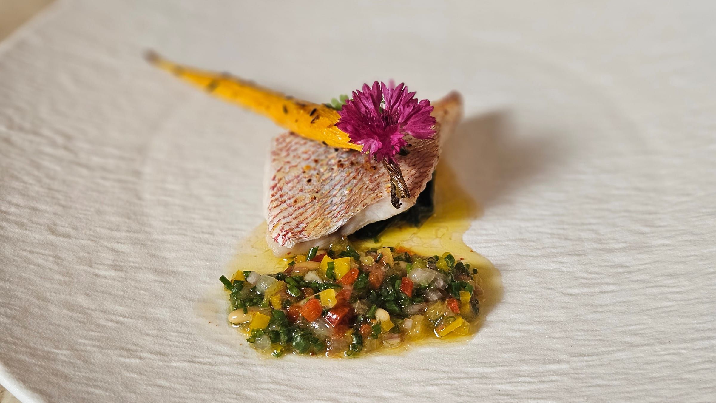 A plated fish course finished with fresh herbs.