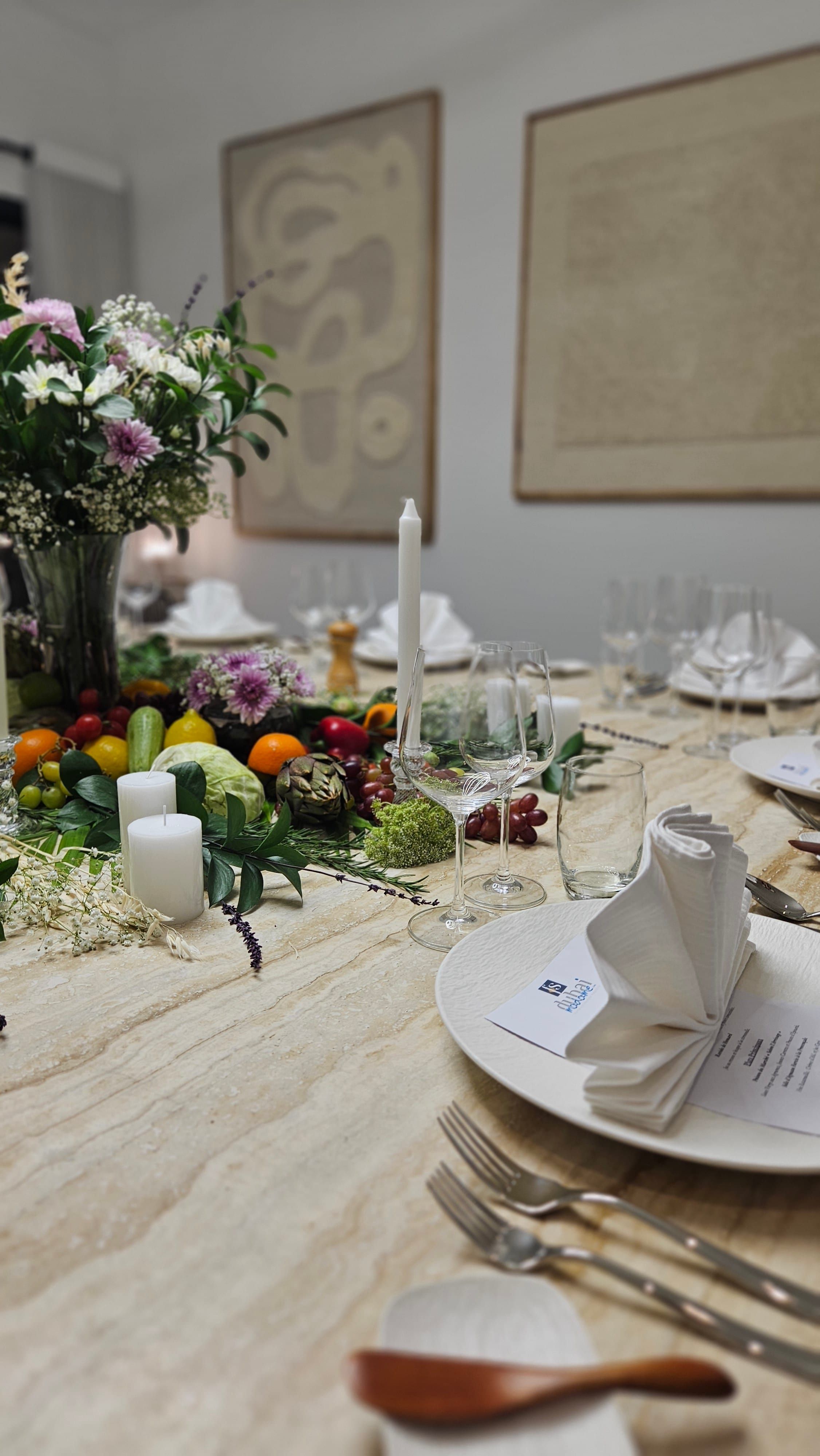 A dining table dressed for a yacht dinner in Dubai, with a centrepiece of flowers, candles and fresh produce.