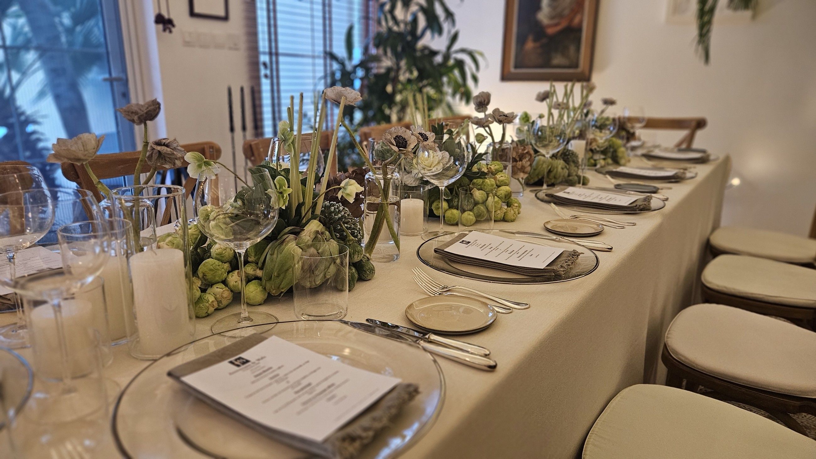 A long dinner table dressed with greenery and printed menus.