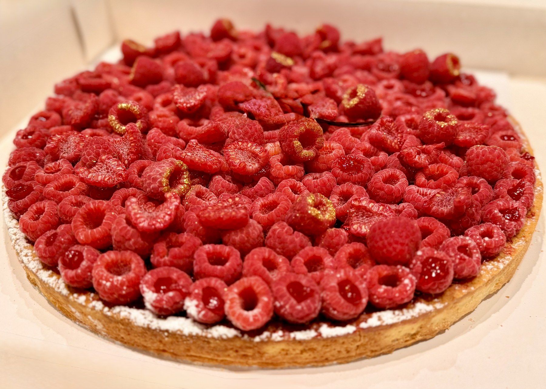 Fresh raspberry tart with gilded berries and rose petals.